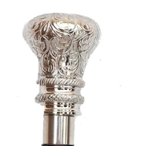 May include: A silver-colored walking cane with an ornate, floral-patterned handle. The handle is bulbous and detailed, with a textured design. The cane's shaft is a polished silver color, and the overall design is elegant.