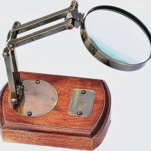 May include: A vintage magnifying glass with a brass frame and a wooden base. The adjustable arm allows for flexible positioning of the lens. The base has a brass plate and a circular brass accent.