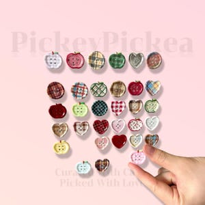 May include: A collection of decorative buttons in various shapes, including apples and hearts. The buttons feature diverse patterns such as plaid, gingham, and solid colors. The image includes the text "PickeyPickea" and "Curated with Care, Picked With Love".