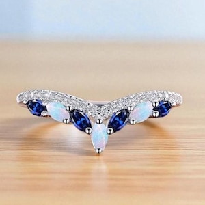 Peut inclure: Une bague argentée avec un design incurvé. La bague présente une rangée de petites pierres claires le long du bord supérieur. Le centre de la bague est orné de pierres précieuses ovales bleues et blanches alternées.