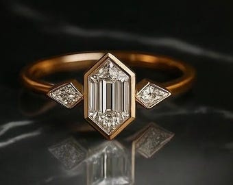 May include: A gold ring with a central emerald-cut diamond, flanked by two smaller diamond accents. The ring's design features a geometric, Art Deco style, set against a dark, reflective surface.