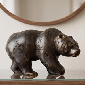 May include: A dark brown bear figurine crafted with a textured finish that mimics fur. The bear is depicted in a walking stance, with its head turned slightly to the right, showcasing detailed facial features including ears, eyes, and a snout.