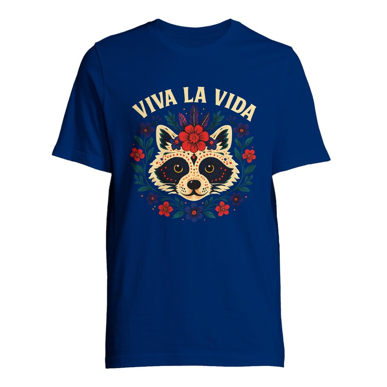 May include: A royal blue t-shirt featuring a raccoon design with a floral wreath and the text "VIVA LA VIDA" in a decorative font. The raccoon has a sugar skull-inspired design with red flowers and accents. The shirt is a short-sleeved crew neck.