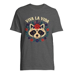 May include: Dark gray t-shirt featuring a raccoon face design with a floral wreath and the text "VIVA LA VIDA" in yellow. The raccoon has a decorative face with a red flower crown. The design includes red, blue, and yellow flowers.