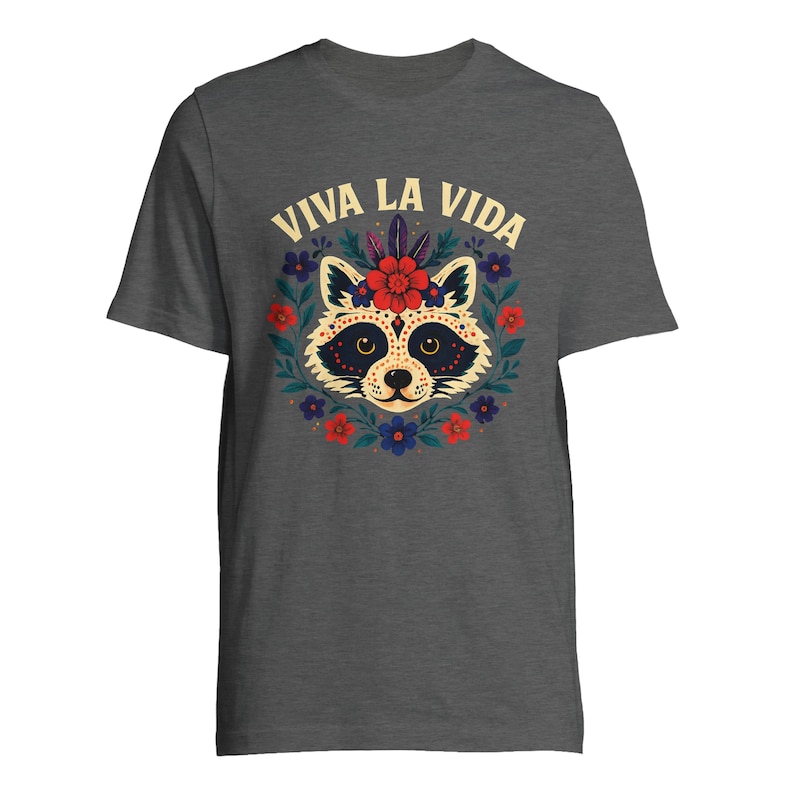 May include: Dark gray t-shirt featuring a raccoon face design with a floral wreath and the text "VIVA LA VIDA" in yellow. The raccoon has a decorative face with a red flower crown. The design includes red, blue, and yellow flowers.