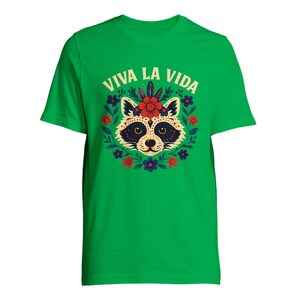 May include: Green t-shirt featuring a raccoon design with a floral wreath and the text "VIVA LA VIDA" in white. The raccoon has a decorative face with a flower crown. The shirt is a vibrant green color.