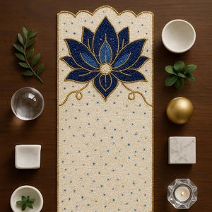 Puede incluir: Un camino de mesa color crema con un diseño de cuentas que presenta flores de loto azules y detalles dorados. El camino de mesa está rodeado de elementos decorativos, como cuencos pequeños, cubos de mármol y una esfera de cristal.