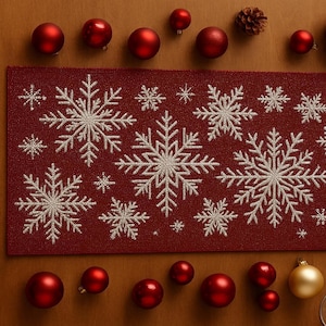 Puede incluir: Un camino de mesa burdeos con copos de nieve blancos bordados. Adornos navideños rojos y un adorno dorado están esparcidos alrededor del camino de mesa. También hay copas de vino presentes, lo que sugiere un tema festivo de vacaciones.