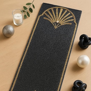 Peut inclure: Chemin de table rectangulaire noir avec des motifs en forme d'éventail en perles dorées à chaque extrémité et une bordure en perles dorées. Des perles décoratives et des objets noirs en forme de nœud sont disposés autour du chemin de table.