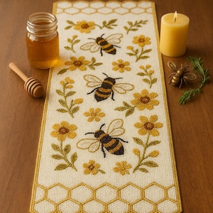 May include: A cream-colored table runner with a bee and honeycomb design. The runner features embroidered bees, yellow flowers, and a honeycomb border. A jar of honey, a honey dipper, and a candle are on the table.