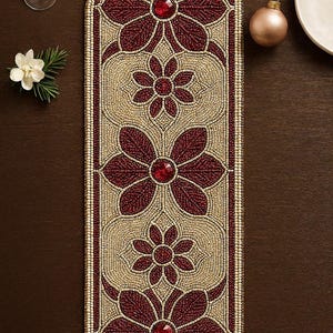 Może przedstawiać: Bieżnik na stół z koralików z kwiatowym wzorem. Bieżnik ma powtarzający się wzór bordowych kwiatów z czerwonymi kamieniami szlachetnymi na beżowym tle. Krawędzie są obszyte kremową obwódką. Idealny do dekoracji wnętrz.