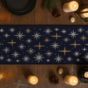 May include: A navy blue table runner featuring a repeating pattern of gold and silver stars. The rectangular runner is likely fabric. The stars are of varying sizes and designs, creating a festive, celestial theme for a dining table.