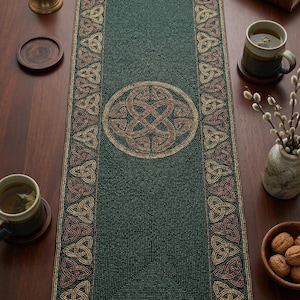 May include: A dark green beaded table runner with a Celtic knot design. The runner has a central circular knot and borders with repeating knot patterns in shades of brown and gold. The runner is on a dark wooden table.