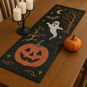 Puede incluir: Camino de mesa negro de Halloween con diseños bordados de calabaza naranja, fantasma, murciélago y árboles. Una pequeña calabaza naranja está sobre la mesa. Un candelabro negro con tres velas blancas está sobre la mesa.