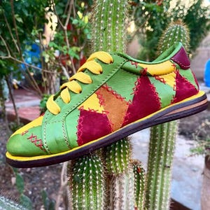 以下が含まれることがあります： 緑、黄色、バーガンディ色の革パネルを使用した、カラフルなパッチワークスニーカー。 黄色の靴紐と茶色のソールが特徴です。 デザインにはステッチのディテールが組み込まれており、ユニークで手作りの外観を作り出しています。 ローカットスタイルです。