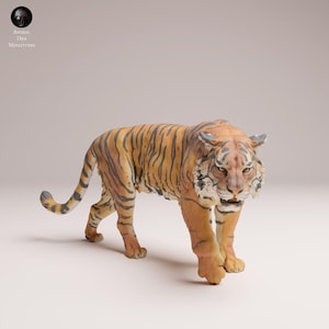 Può includere: Statuetta dettagliata di una tigre, con pelliccia arancione e strisce nere. La tigre è raffigurata in posizione di camminata, mostrando la sua corporatura muscolosa e le sue caratteristiche realistiche. La statuetta ha un volto dettagliato ed è etichettata "Animal Des Miniatures".