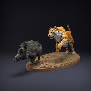 Può includere: Statuetta dettagliata raffigurante una tigre e un cinghiale su una base ovale marrone. La tigre è arancione con strisce nere, in posa di caccia. Il cinghiale è grigio e rivolto verso la tigre. La base ha un aspetto sabbioso strutturato.