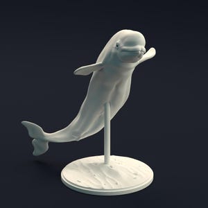 Könnte beinhalten: Eine weiße Beluga-Wal-Skulptur, montiert auf einem Ständer. Der Wal ist in einer dynamischen Pose dargestellt, mit gebogenem Körper und ausgestreckten Flossen. Der Sockel ist kreisförmig mit strukturierter Oberfläche, die Sand andeutet. Dunkler Hintergrund.