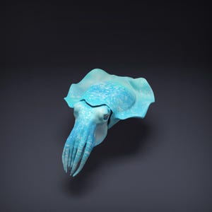 Könnte beinhalten: Eine detaillierte, hellblaue Skulptur eines Tintenfischs. Der Kopffüßer hat einen gerüschten Mantel, strukturierte Haut und mehrere Tentakel. Die Skulptur ist vor einem dunkelgrauen Hintergrund platziert, der seine aquatische Form hervorhebt.