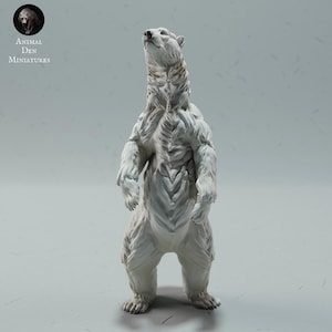 Peut inclure: Figurine d'ours polaire blanc debout, regardant vers le haut. L'ours présente une texture de fourrure détaillée et une musculature. Le logo Animal Den Miniatures est visible en haut à gauche.