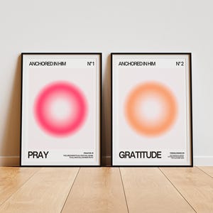 May include: Two framed art prints with black borders. One features a pink and white gradient circle with the word "PRAY" below. The other has an orange and white gradient circle with the word "GRATITUDE". Both prints have the text "ANCHORED IN HIM" at the top.