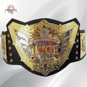 Könnte beinhalten: Ein schwarzer Meisterschaftsgürtel mit einer großen, verzierten Gold- und Silberplatte in der Mitte mit dem Text IWGP WORLD HEAVYWEIGHT CHAMPION. Die Platte ist mit kleinen roten und klaren Edelsteinen, Gravuren und Seitenplatten verziert.