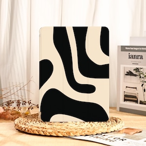 May include: A tablet case with a cream-colored background and bold black abstract shapes. The case is rectangular and appears to be made of a smooth material. The design is modern and eye-catching, suitable for protecting a tablet.