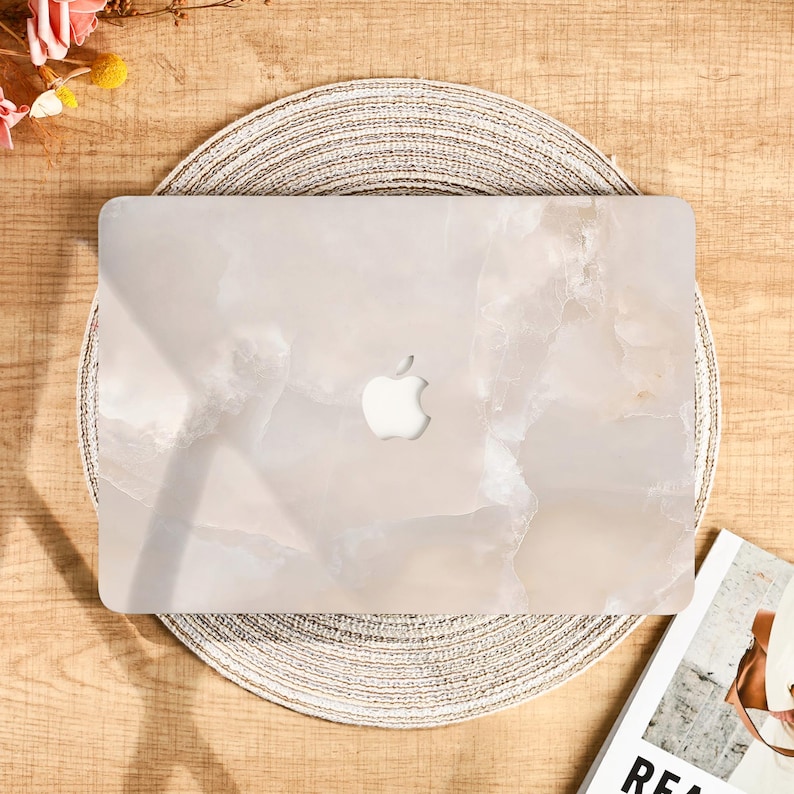 Peut inclure: Un ordinateur portable clair avec un motif semblable &agrave; du marbre, orn&eacute; du logo Apple. L'ordinateur est pos&eacute; sur un dessous-de-plat rond et tiss&eacute;. L'esth&eacute;tique g&eacute;n&eacute;rale est neutre et moderne.