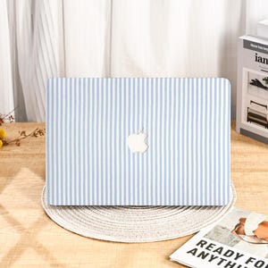 Könnte beinhalten: Eine Laptop-Hülle mit blau-weißem Streifenmuster. Das Apple-Logo ist mittig zu sehen. Die Hülle liegt auf einem runden, gewebten Platzset.