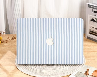 Peut inclure: Une coque d'ordinateur portable à rayures bleues et blanches. Le logo Apple est visible au centre. La coque est posée sur un dessous de plat rond et tissé.