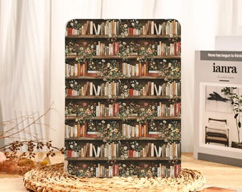 May include: A tablet case featuring a repeating pattern of a bookshelf filled with books and flowers. The design includes various book colors and floral arrangements, set against a dark brown background. The case is on a woven mat.