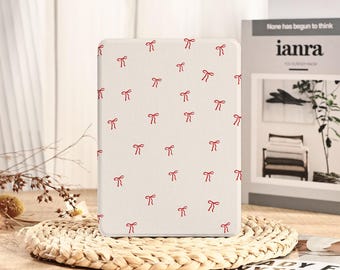 Puede incluir: Una funda rectangular blanquecina con un patrón repetido de pequeños lazos rojos. La funda está sobre una esterilla tejida. El fondo incluye el texto "None has begun to think" y "ianra".