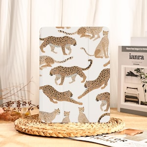 Puede incluir: Funda blanca para tableta con un patrón repetido de leopardos estilizados en varias poses. Los leopardos están representados en tonos marrones y beige con manchas negras. La funda es rectangular y parece estar hecha de un material liso.