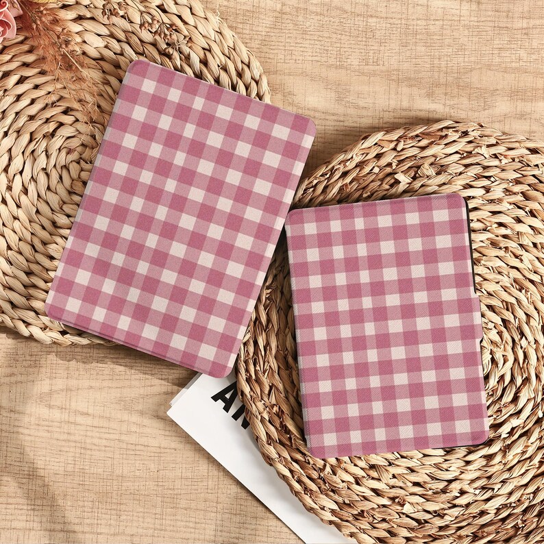 May include: Two notebooks with a pink and white gingham pattern are displayed on a woven surface. The notebooks are open, revealing the pattern on the cover. The background includes a natural woven texture.
