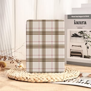 May include: A rectangular case with a plaid pattern in brown, pink, and cream colors. The case is resting on a woven placemat. In the background, a framed print and a plant are visible.
