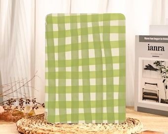 May include: A green and white checkered pattern tablet case. The case is rectangular and has a light green and white gingham design. The case is sitting on a woven placemat. The text "ianra" is visible on a book in the background.