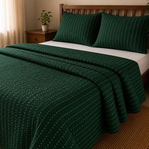 Puede incluir: Una colcha de color verde bosque oscuro y dos fundas de almohada a juego con un patrón de costuras blancas verticales. El juego de cama se muestra sobre una cama con una sábana blanca, cubriendo el colchón y las almohadas con un diseño acolchado.