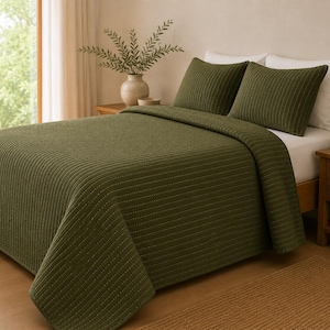 May include: An olive green quilt with a textured, vertical channel-stitched pattern covering the entire surface. The set includes two matching rectangular pillow shams featuring the same ribbed design, placed over white pillows on a bed frame.