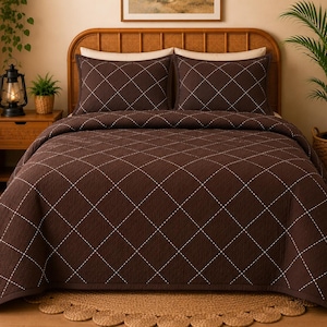 Peut inclure: Un couvre-lit marron foncé et deux taies d'oreiller assorties présentant un motif de losanges cousus en blanc. La parure de lit est drapée sur un cadre de lit à tête arrondie, affichant une texture matelassée uniforme sur toutes les pièces.