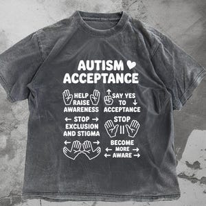 May include: A gray t-shirt with the words "AUTISM ACCEPTANCE" in white, along with hand illustrations and phrases like "Help Raise Awareness" and "Say Yes to Acceptance." The shirt has a vintage, washed look.