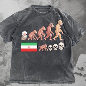 Puede incluir: Camiseta gris oscuro con un gráfico que representa la evolución humana, comenzando con una figura con turbante y terminando con un humano. El diseño también incluye la bandera iraní y varias calaveras.
