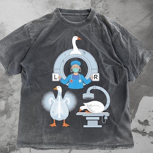 Könnte beinhalten: Dunkelgraues T-Shirt mit einem humorvollen medizinischen Motiv. Das Design zeigt eine Cartoon-Gans, die sich einer Röntgenaufnahme unterzieht, eine Arzt-Gans und eine Gans mit sichtbaren Knochen. Die Buchstaben "L" und "R" sind ebenfalls vorhanden.