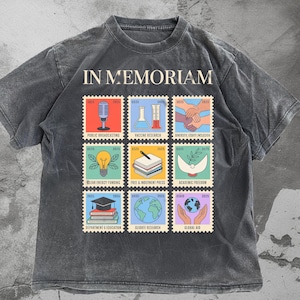 May include: Dark grey t-shirt with the words "IN MEMORIAM" above nine postage stamp-style graphics. Each graphic features a different image and text, including a microphone, a beaker, and a globe. The shirt is made of a soft, comfortable material.