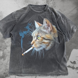 Può includere: T-shirt grigio scuro con grafica dettagliata di un gatto con occhi verdi che fuma una sigaretta. Il gatto ha pelo marrone e marrone chiaro, con fumo blu. La maglietta ha girocollo e maniche corte.