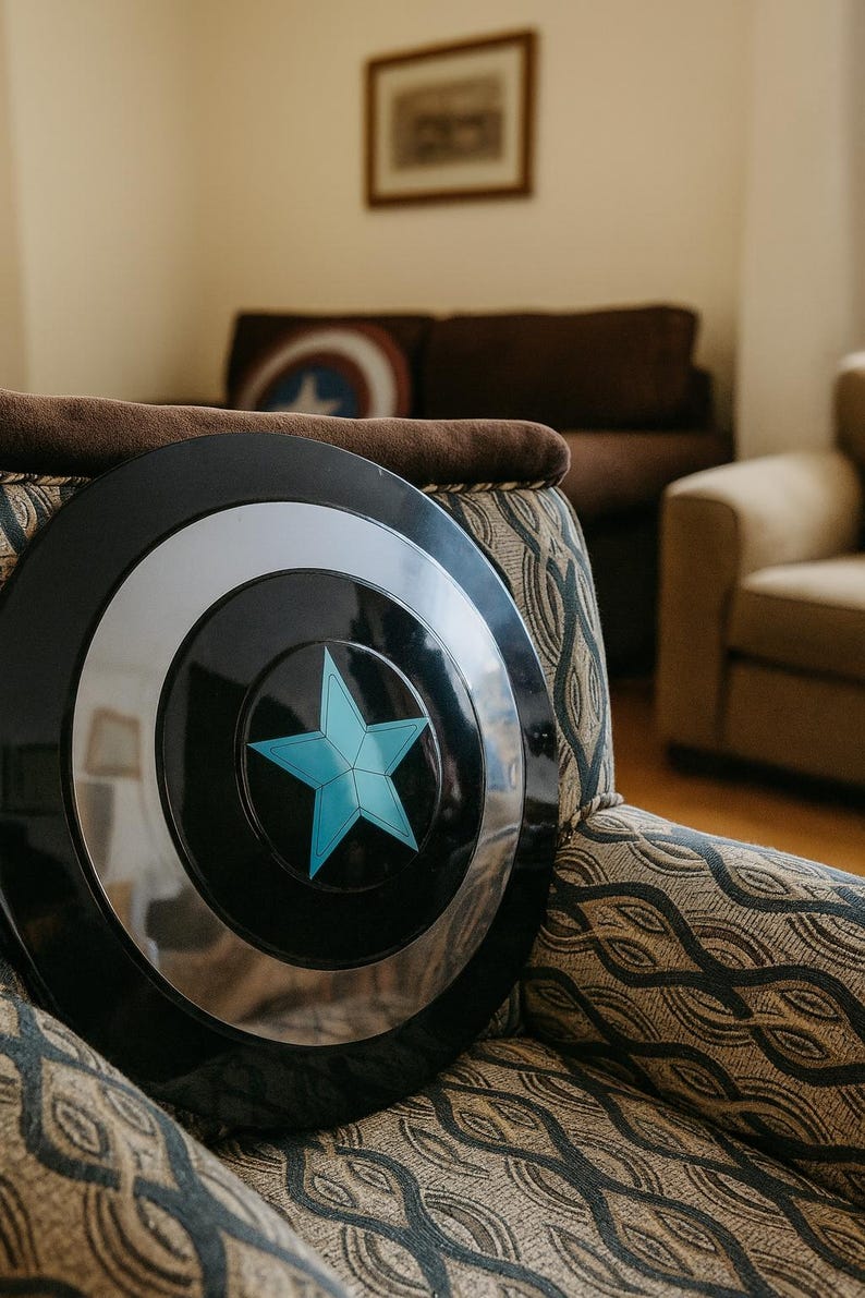 May include: A black and silver shield with a blue star emblem, resting on a patterned armchair. The shield has a circular design with a silver ring and a central blue star. The armchair has a brown cushion and a patterned fabric.