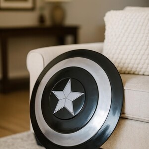 May include: A black, silver, and white shield with a star emblem. The shield is round with a black outer ring, a silver middle ring, and a black center with a white star. The shield is leaning against a beige couch.