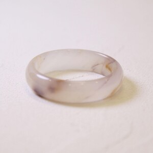 Op de afbeelding: Een doorschijnende, lichtpaarse ring met subtiele bruine en witte marmering. De gladde, afgeronde band is een eenvoudig, elegant ontwerp. Deze ring is een sieraad.