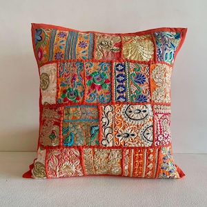 May include: Square decorative pillow with a patchwork design. The pillow features a vibrant mix of colors including orange, gold, blue, and pink. The patchwork is made up of various embroidered and textured fabrics, creating a unique and eye-catching design.