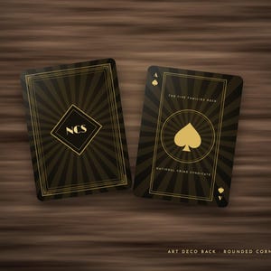 May include: Two playing cards with a black and gold sunburst design. The left card features a diamond shape with the letters NCS. The right card displays a spade symbol, the text The Five Families Deck, and National Crime Syndicate.