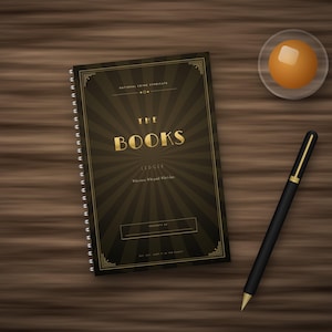 May include: A spiral-bound notebook with a dark brown cover featuring a gold sunburst pattern and the text THE BOOKS LEDGER. A black pen with gold accents and a small glass dish containing a round orange object are positioned nearby.